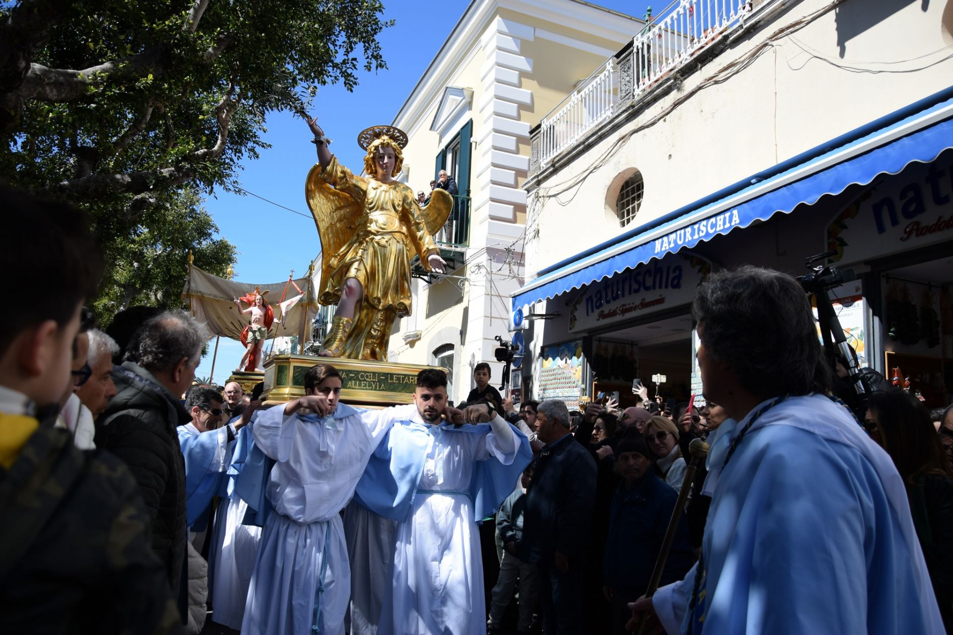 Una scena suggestiva della Corsa dell'Angelo. Al centro della scena, l'Angelo si erge con un gesto di annuncio, comunicando a Maria la Resurrezione di Cristo. La scena si svolge nella piazza, circondata dalla folla, che partecipa con devozione ed emozione a questo momento di profonda spiritualità.
