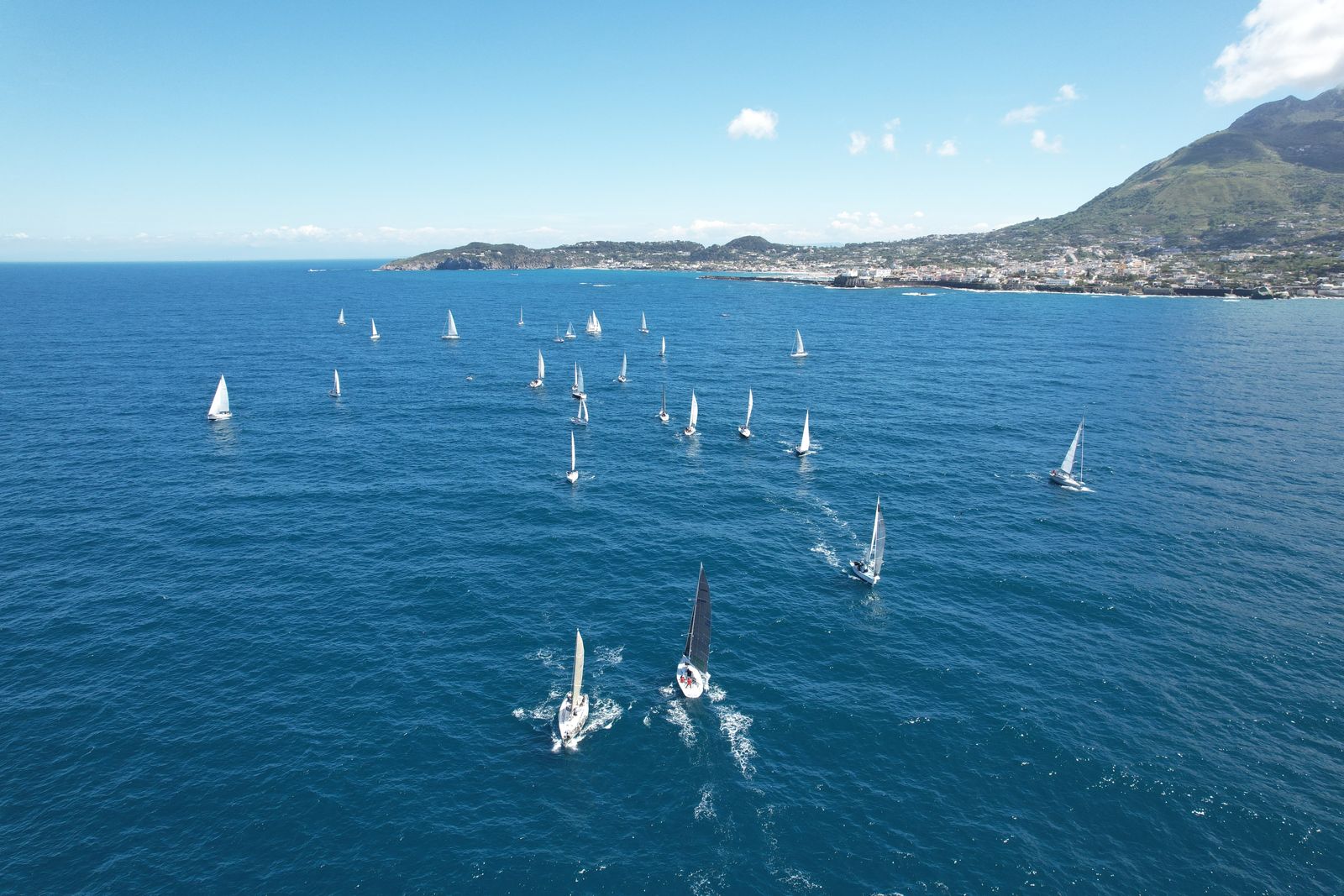 Una panoramica suggestiva delle vele che partecipano alla regata di 24 ore, con l'isola visibile in lontananza