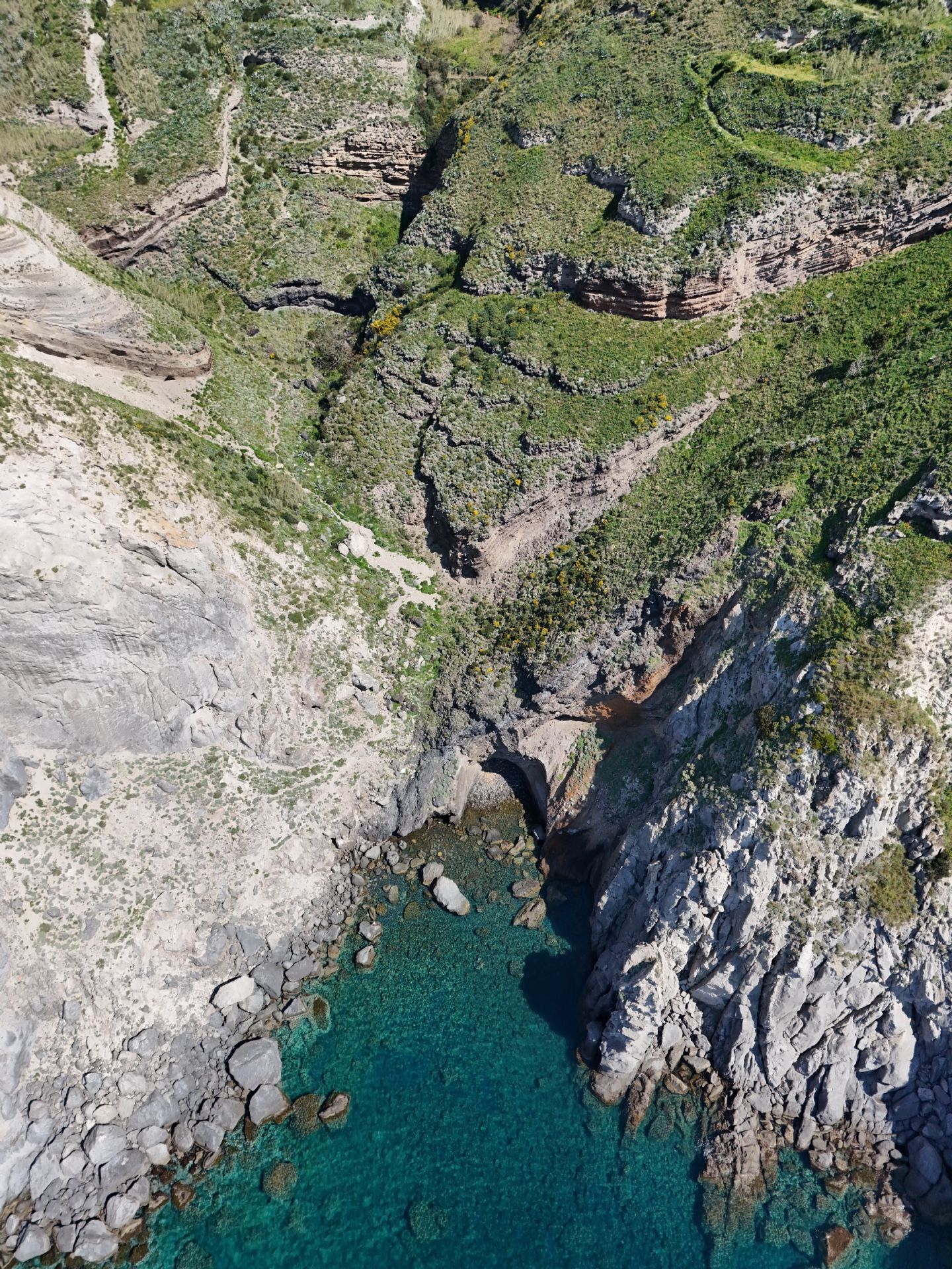 Un sentiero immerso nel verde, tra rocce e piante, che si affaccia su un mare cristallino, conducendo a una tranquilla baia nascosta.