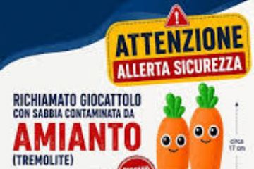 giocattolo a forma di carota sorridente, arancione con ciuffo verde. Scritta di allarme Richiamo giocattolo con sabbia contaminata da amianto.